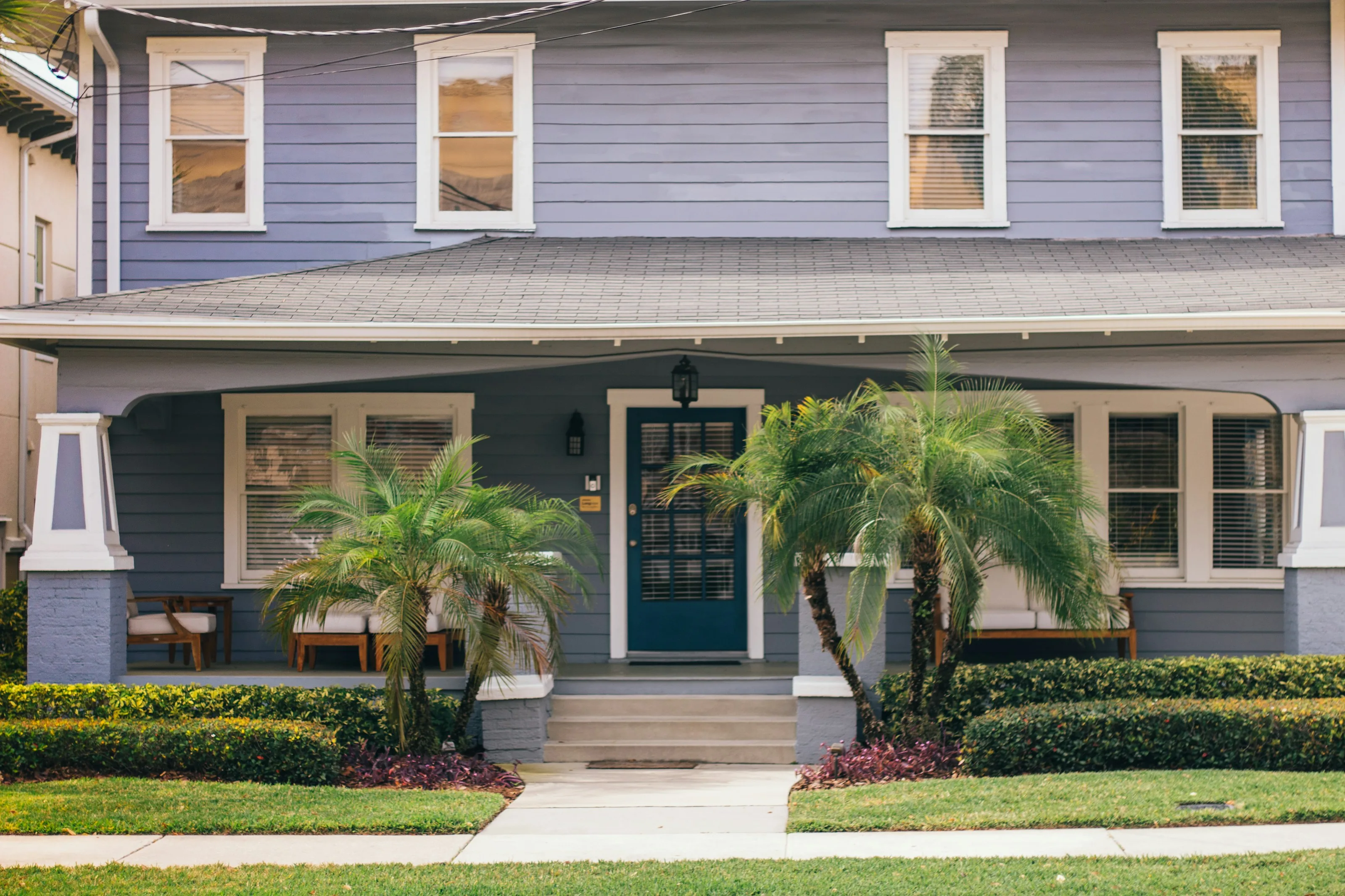 Blue clapboard house with a front porch and palm trees
