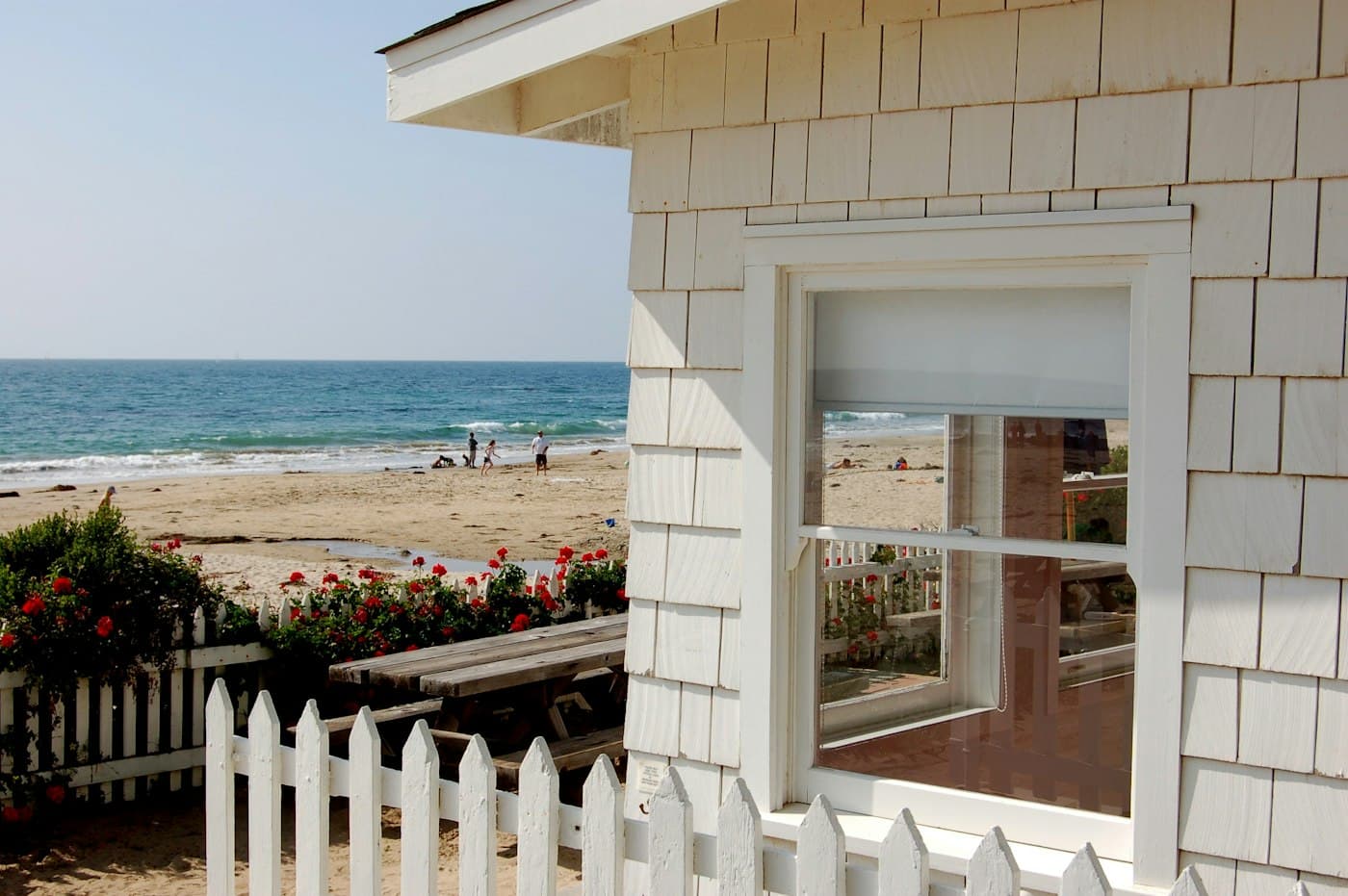 White shingled cottage with a picket fence overlooking the beach